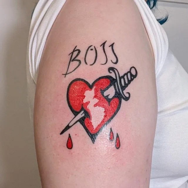 Red heart pierced by a dagger with the word BOSS above it, on an upper arm