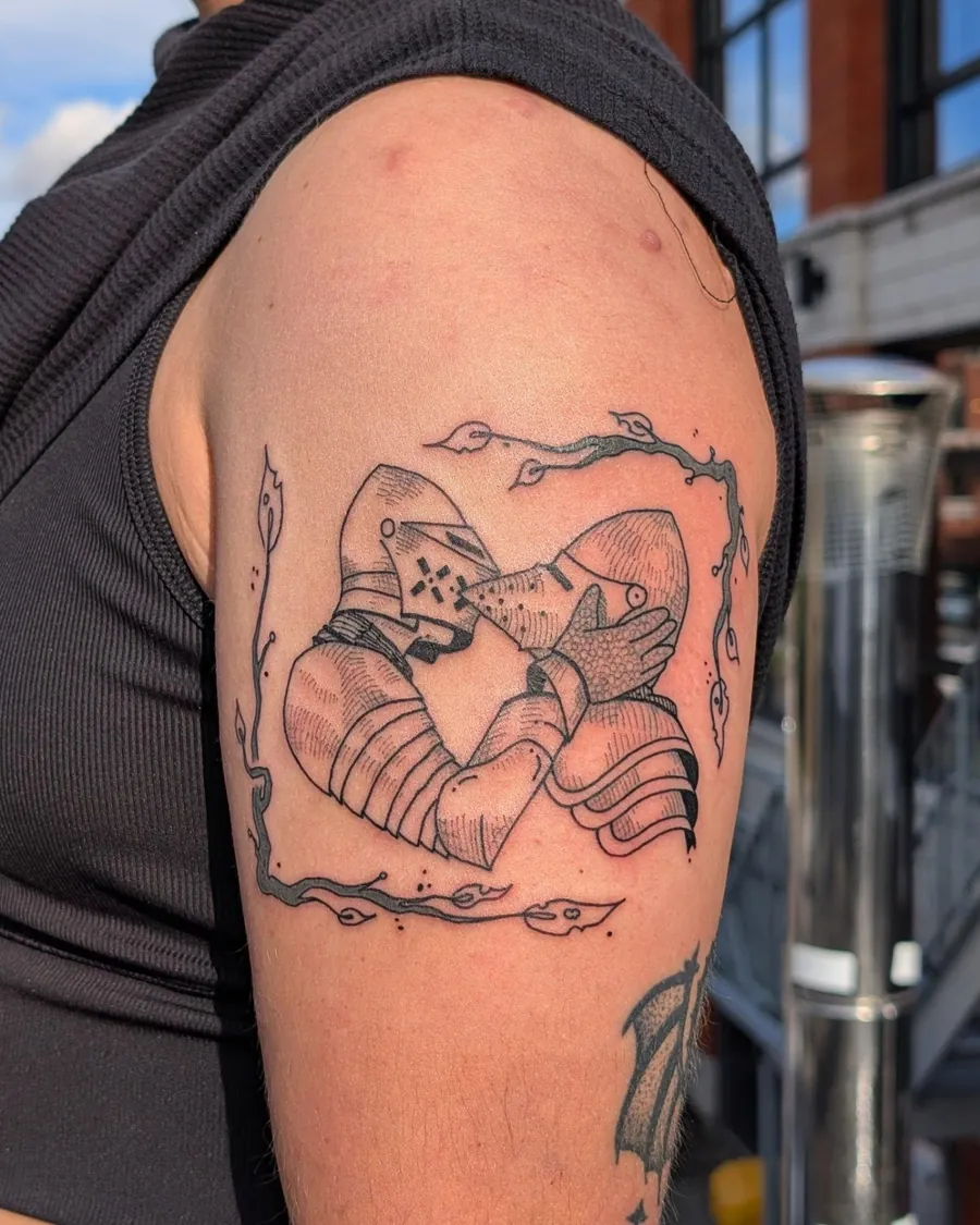 Linework tattoo of two armoured knights embracing inside a thorny frame, on an upper arm
